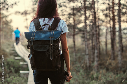Back view of a tourist girl with backpack walk on a wooden footpath in beautiful forest.