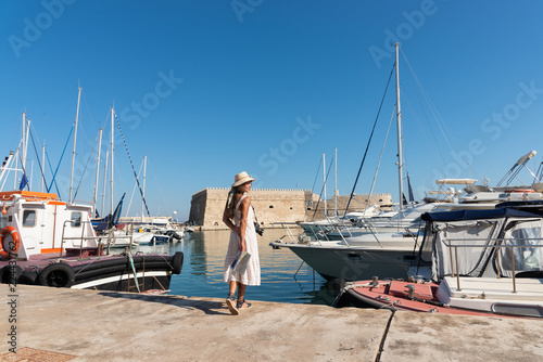 Elegant young tourist visitor woman walking on a sightseeing tour at Heraklion Venetian port, Crete, Greece 