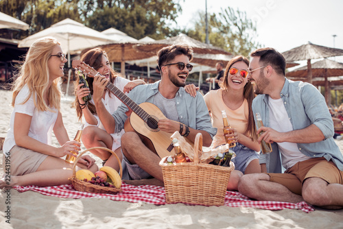 Group of friends with guitar having fun on the beach