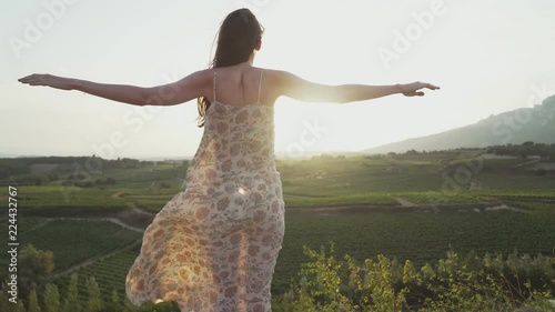 Slender woman stands on top, straightening her arms, she looks at the beautiful landscape, and her dress develops in the wind