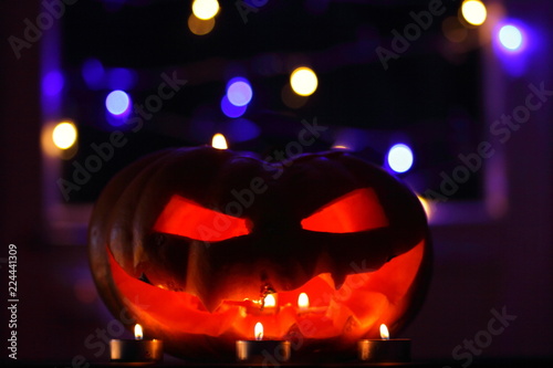 Halloween pumpkin. Candles, bat and glowing pumpkin. Halloween with colorful bokeh. Atmosphere for holiday. Pumpkin on wooden boards against background of colored garlands