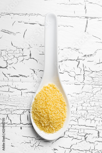 Heap of raw, uncooked couscous in white spoon on wooden table photo