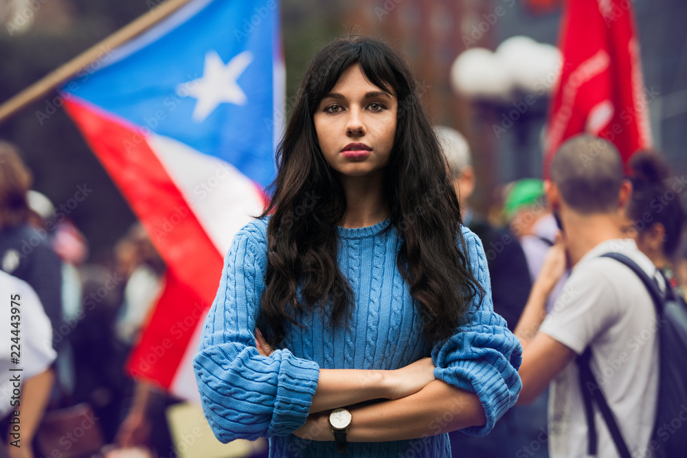 Beautiful activist woman protesting on city street with arms crossed