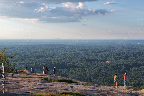 Several unidentifiable people looking out over the green trees and forests visible from the top of Stone Mountain in Georgia on a lovely summer day