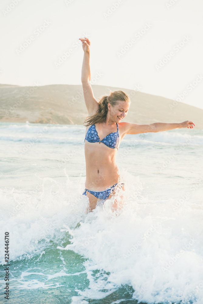 Young beautiful blond woman tourist jumping and smiling in wavy waters of Mediterranean sea in Prasonisi cape, Rhodes, Greece Young beautiful blond woman tourist jumping and smiling in wavy waters of Mediterranean sea in Prasonisi cape, Rhodes, Greece