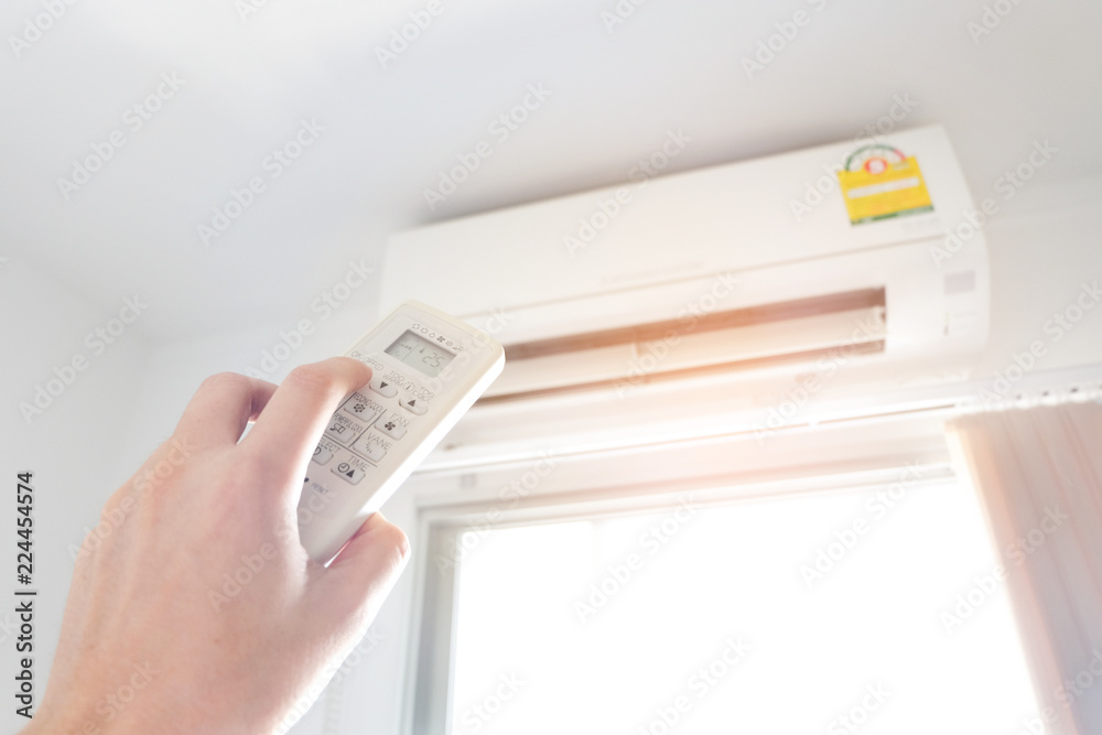 Man's hand using remote control open The air conditioner is cooled to 25 degrees Celsius in his bedroom. Health concepts and energy savings