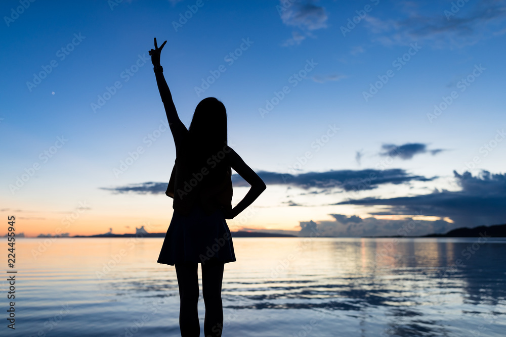 Silhouette of woman showing victory sign with the background of sea and sunset