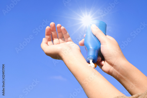 Hand of female holding sunscreen. Very sun light Sky background.Health concepts and skin care