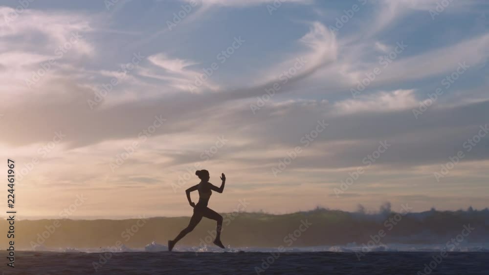 silhouette woman running on beach waves splashing female athlete runner exercising sprinting intense workout on rough ocean seaside at sunset