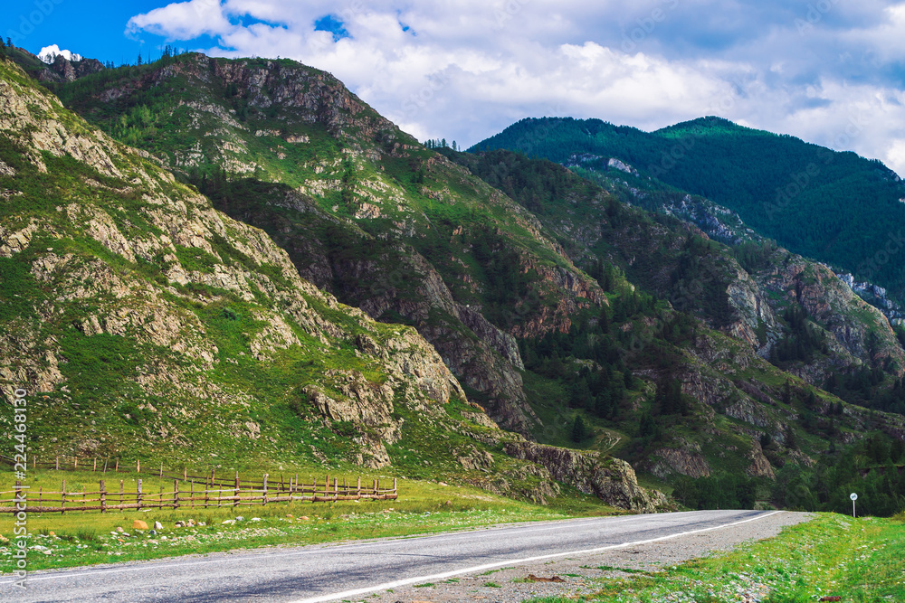 Mountain highway across pass in sunlight. Asphalt road near foot of giant mountains. Amazing colorful highland landscape of majestic nature.