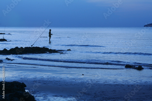 Black silhouettes of men fishing at sea in the evening.