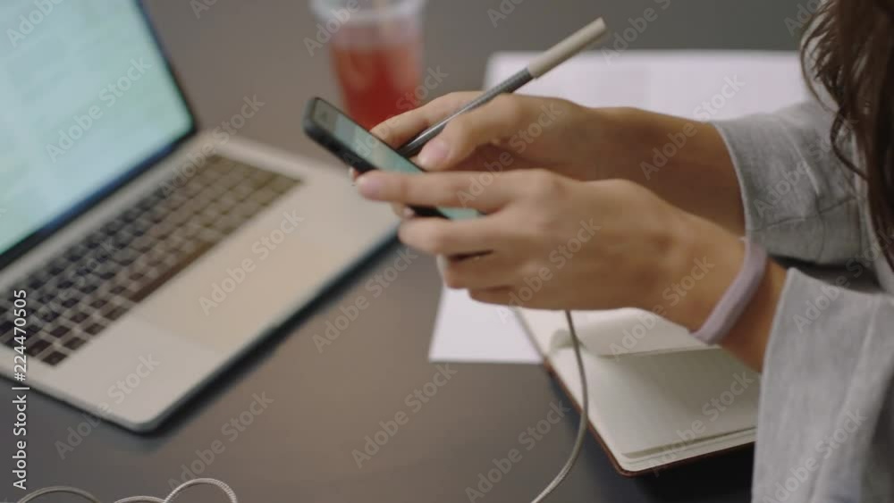 young asian business woman writing notes using smartphone checking messages enjoying study listening to music wearing headphones female student in office workplace close up