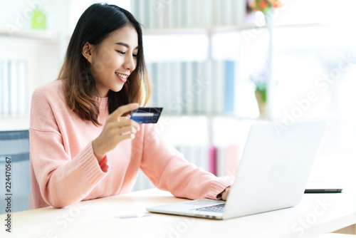 Young attractive asian woman holding credit card sitting at table typing keyboard on laptop computer to shopping online at home office or library. Happy girl student buy and pay in ecommerce concept.