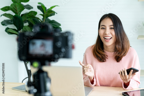 Young attractive asian woman blogger or vlogger looking at camera and talking on video shooting with technology. Social media influencer people or content maker concept in relax casual style at home. photo