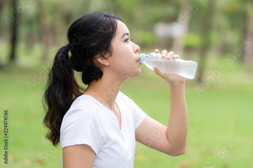 Young woman drinking water form a bottle at park.