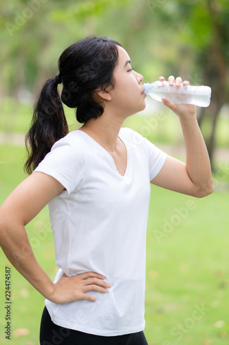 Young woman drinking water form a bottle at park.