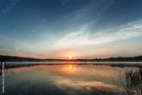 Fototapeta Naklejka Na Ścianę i Meble -  Beautiful, red dawn on the lake. The rays of the sun through the fog. The blue sky over the lake, the morning comes, the sky is reflected in the water.