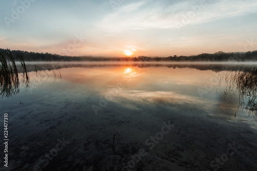 Fototapeta Naklejka Na Ścianę i Meble -  Beautiful, red dawn on the lake. The rays of the sun through the fog. The blue sky over the lake, the morning comes, the sky is reflected in the water.