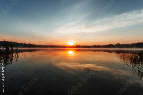 Beautiful, red dawn on the lake. The rays of the sun through the fog. The blue sky over the lake, the morning comes, the sky is reflected in the water.