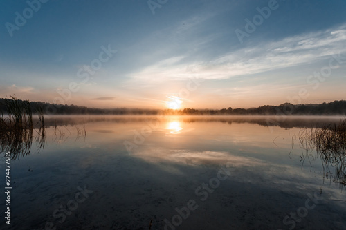 Beautiful, red dawn on the lake. The rays of the sun through the fog. The blue sky over the lake, the morning comes, the sky is reflected in the water.
