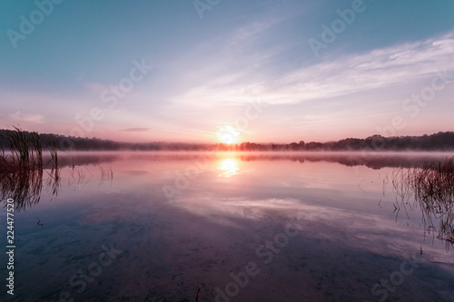 Beautiful  pink violet dawn over the lake. Fog over the lake  the rays of the sun  very dense fog  dawn  the blue sky over the lake  the morning comes  the forest reflects in the water.