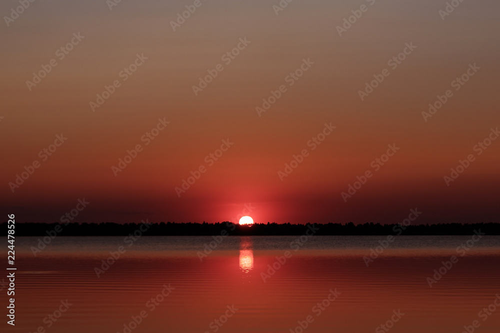 Beautiful, red dawn on the lake. The rays of the sun through the fog. The blue sky over the lake, the morning comes, the sky is reflected in the water.
