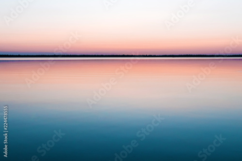 Beautiful, red dawn on the lake. The rays of the sun through the fog. The blue sky over the lake, the morning comes, the sky is reflected in the water.