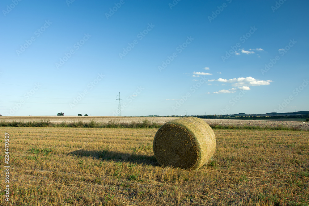 Single round hay bale on stubble, horizon and small cloud on blue sky