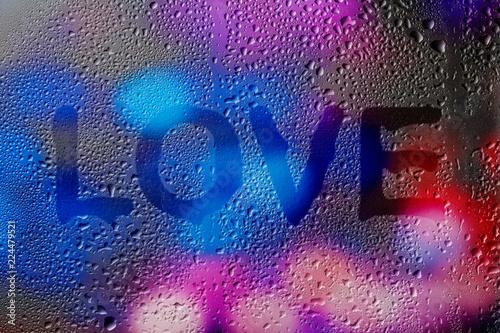 The word Love. Finger written on wet, rainy, steamy window covered with raindrops and colorful bokeh in the background.