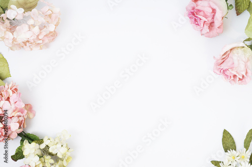 Frame made of pink and beige roses, green leaves, branches on white background. Flat lay, top view. Wedding's background