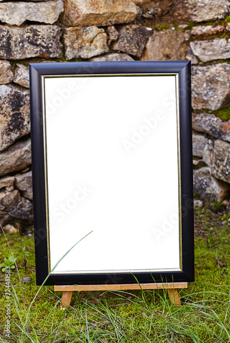 Easel staying om grass and moss near ancient stone walll with copy space
