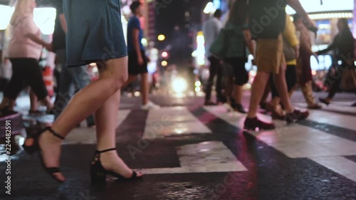 Side view slow motion shot of young businesswoman walking across crowded street at night in Times Square, New York City.