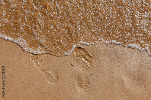 Footprints of bare feet in the sand along a river bank with an oncoming wave