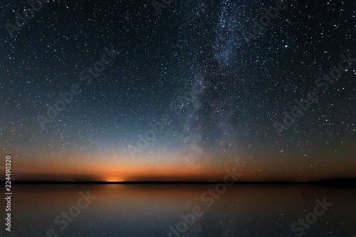 Blue Night Starry Sky With Milky Way Galaxy Above Lake And Russian Village. Night Glowing Stars