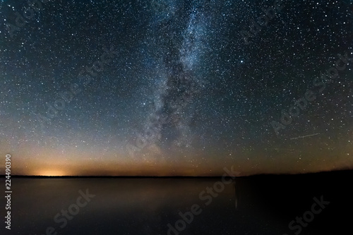 Blue Night Starry Sky With Milky Way Galaxy Above Lake And Russian Village. Night Glowing Stars