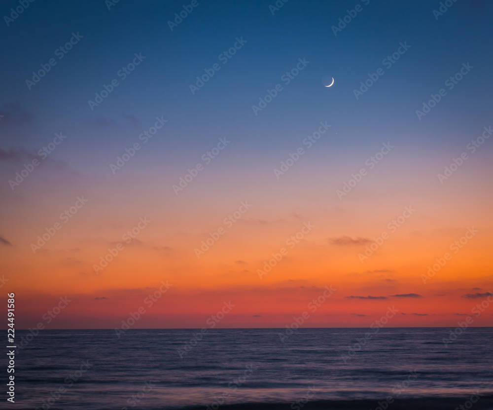 As the sun goes down and seems to melt into the ocean, the skies darken a bit and the moon begins to shine in the seaside sky as friends and lovers sit and enjoy the scene and each other