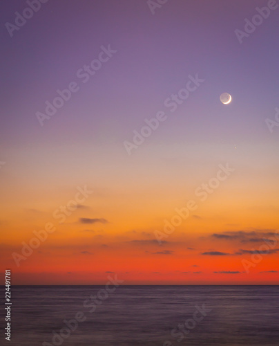 As the sun goes down and seems to melt into the ocean  the skies darken a bit and the moon begins to shine in the seaside sky as friends and lovers sit and enjoy the scene and each other