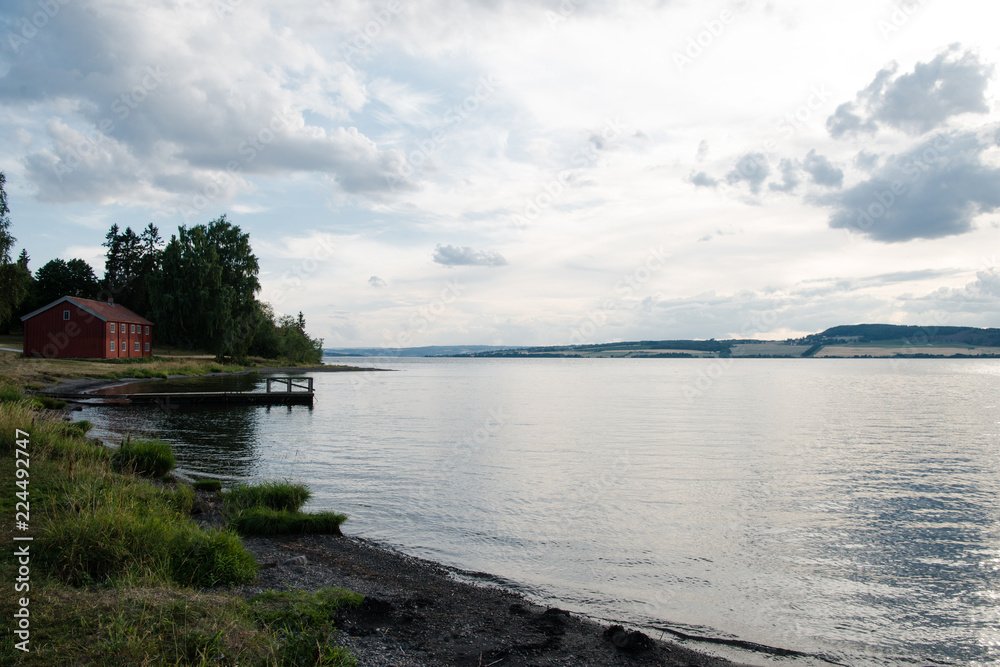 scenic view of Mjosa lake under cloudy sky and distant red cottage, Hamar, Hedmark, Norway