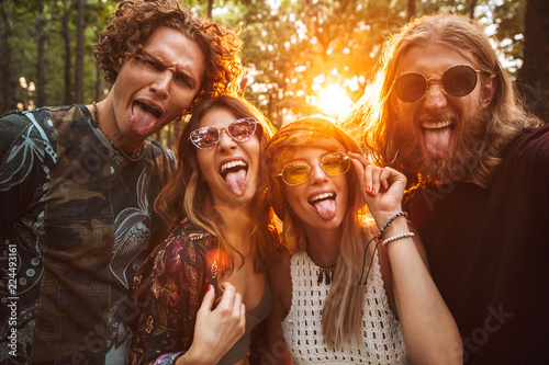 Photo of four hippie people men and women, smiling and taking selfie in forest