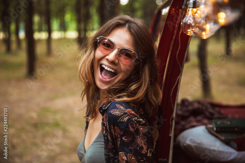 Image of excited woman 20s, wearing stylish accessories smiling while resting in forest camp