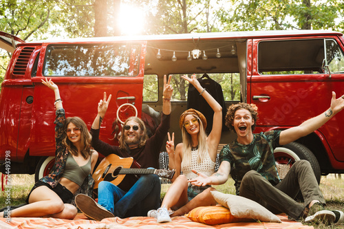 Fotografie Group of young hippies men and women laughing, and sitting near vintage minivan