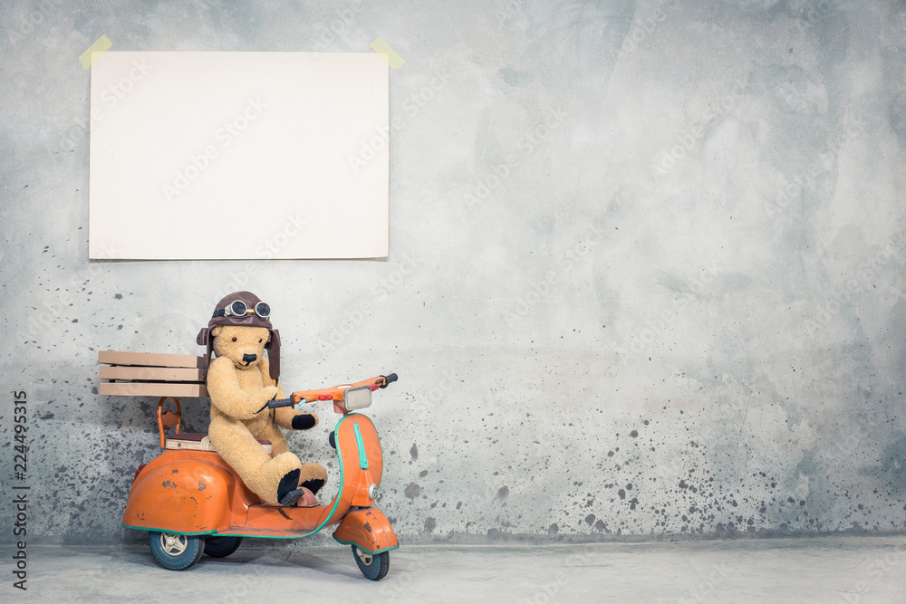 Naklejka premium Miś w kasku pilota skórzanego siedzi na skuter stary zabawka retro pomarańczowy z pudełek pizzy w przedniej betonowej ścianie teksturowanej tle z dużym pustym plakacie papieru. Filtrowane zdjęcie w stylu vintage