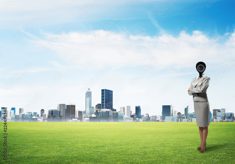 Camera headed woman standing on green grass against modern cityscape Camera headed woman standing on green grass against modern cityscape