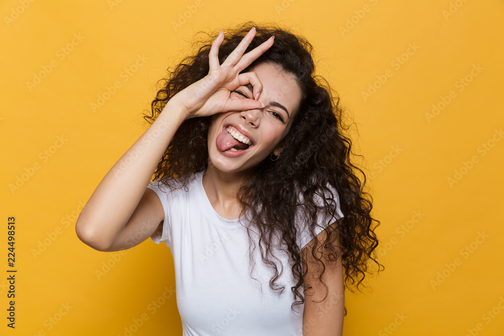 Image of pretty woman 20s laughing and looking at you through hole made by fingers, isolated over yellow background Image of pretty woman 20s laughing and looking at you through hole made by fingers, isolated over yellow background