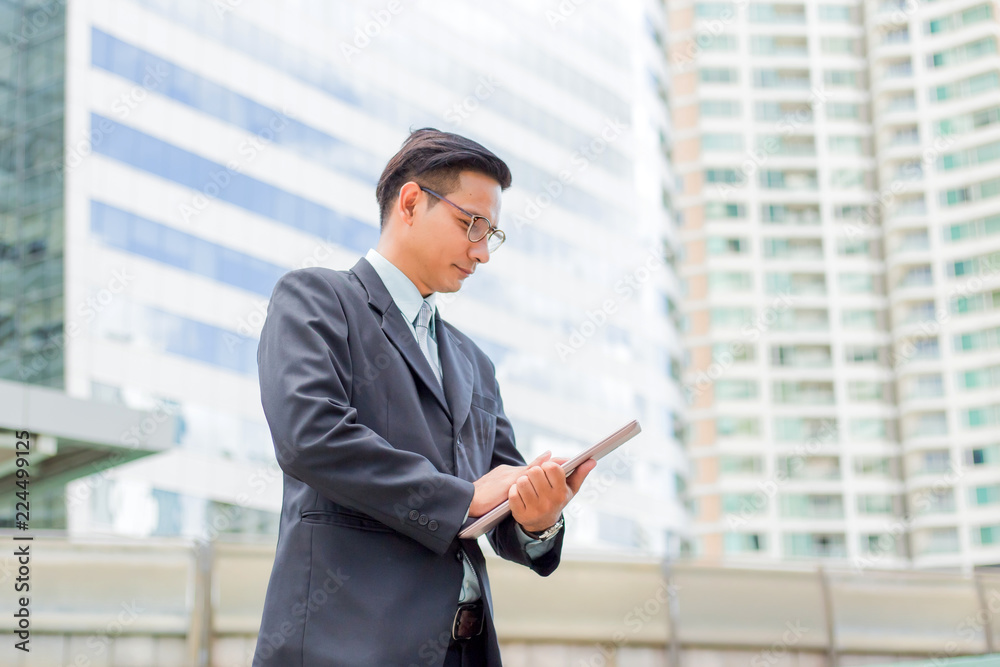Young Asia businessman in suit with his laptop computer outdoors, modern building on the background Young Asia businessman in suit with his laptop computer outdoors, modern building on the background