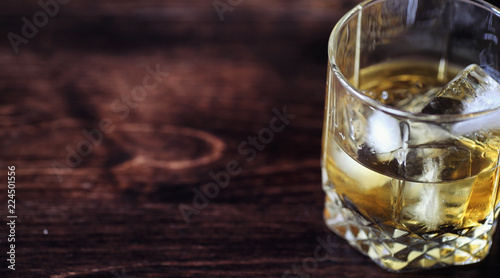 Whiskey with ice with a glass. Cubes of ice on a wooden table an