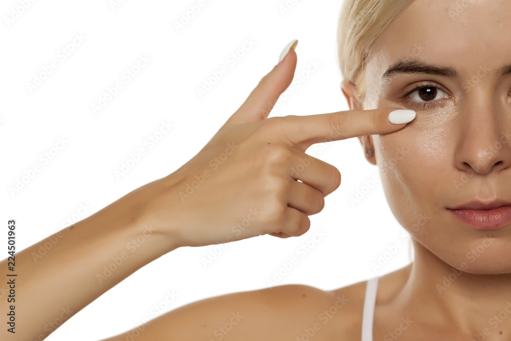 Young woman applying concealer under her eyes with her finger on white background Young woman applying concealer under her eyes with her finger on white background