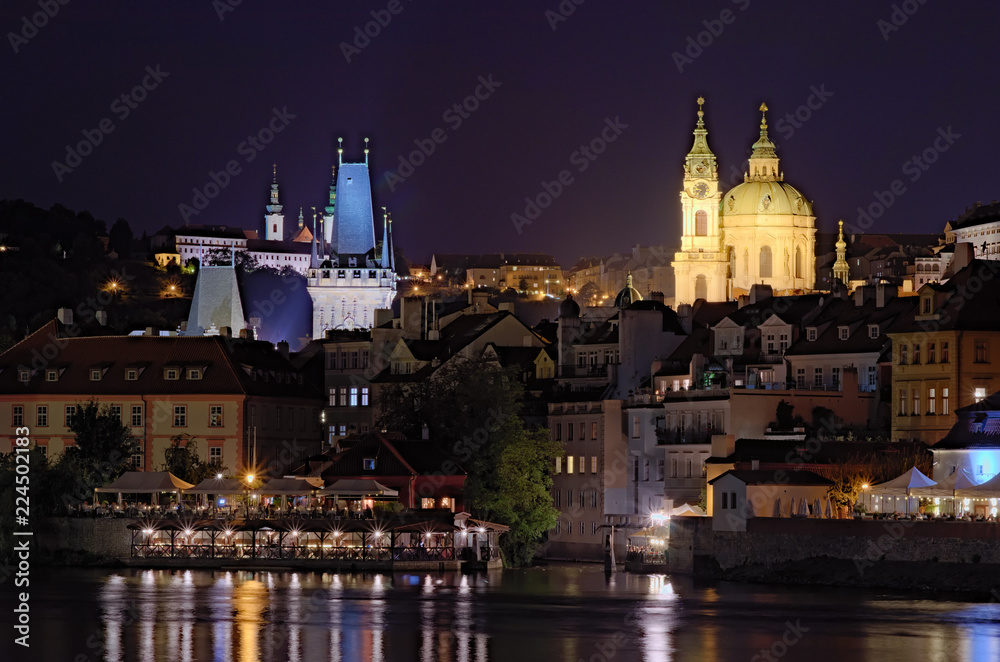 Scenic view of night Prague. Vltava river with many cafes and restaurants in the buildings on the river bank. Medieval buildings of old town at the background at summer night. Prague, Czech Republic