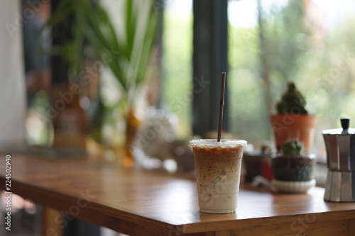 Iced latte coffee in clear plastic cup with brown color strew on timber table