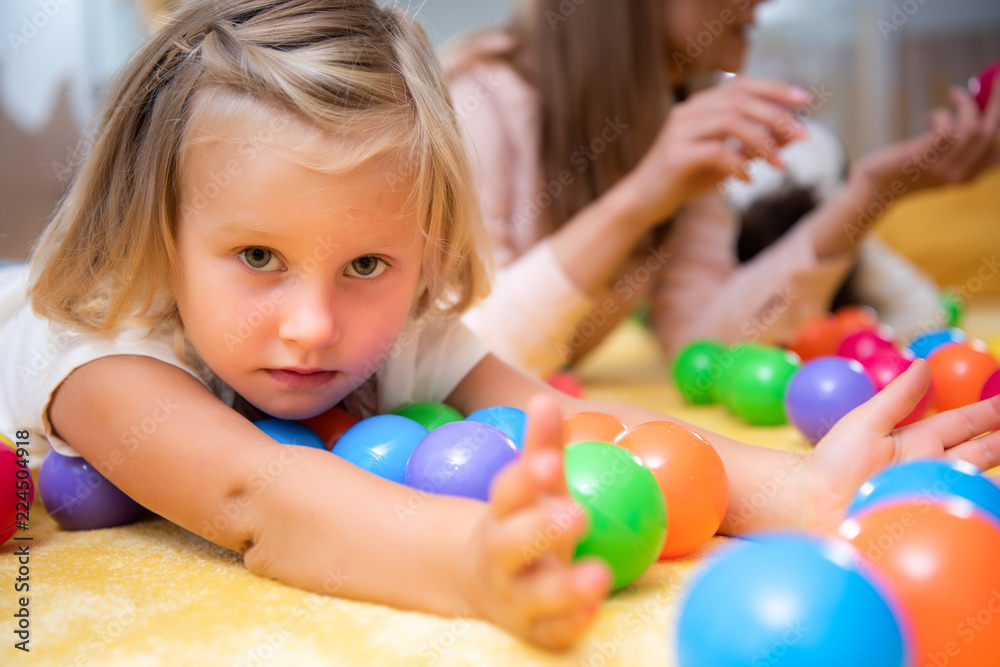 Obraz premium adorable child lying on floor with colored toys and looking at camera in kindergarten